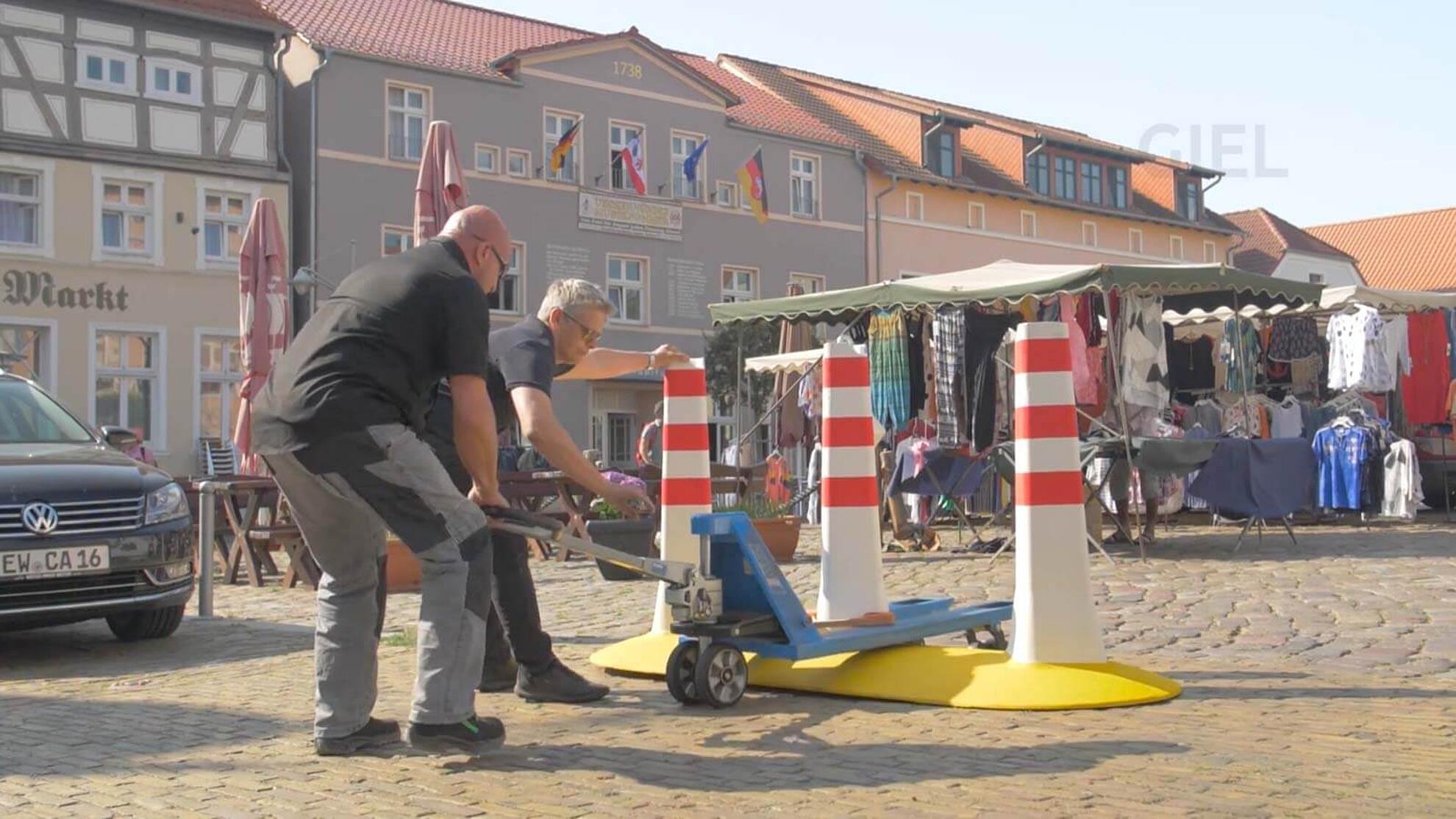 Zwei Männer montieren eine CitySafe Barriere mithilfe von einem Hebewagen.