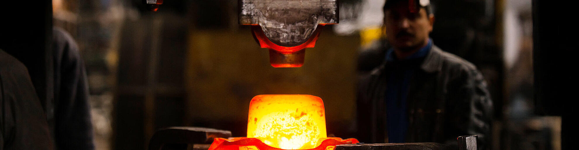 Ein glühendes Stück Metall wird von einem hydraulischen Schmiedehammer geformt.