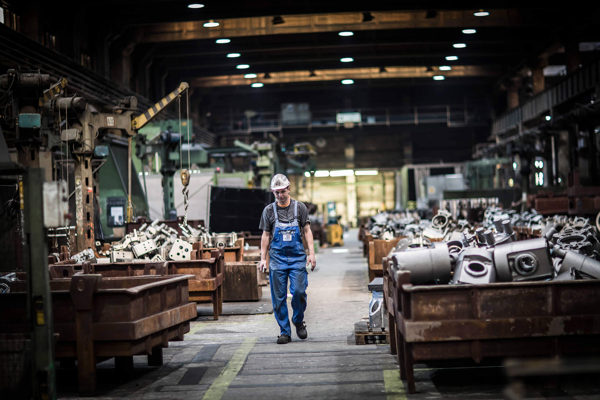 Ein Mitarbeiter steht in einer Lagerhalle voll mit neu angefertigten Bauteilen